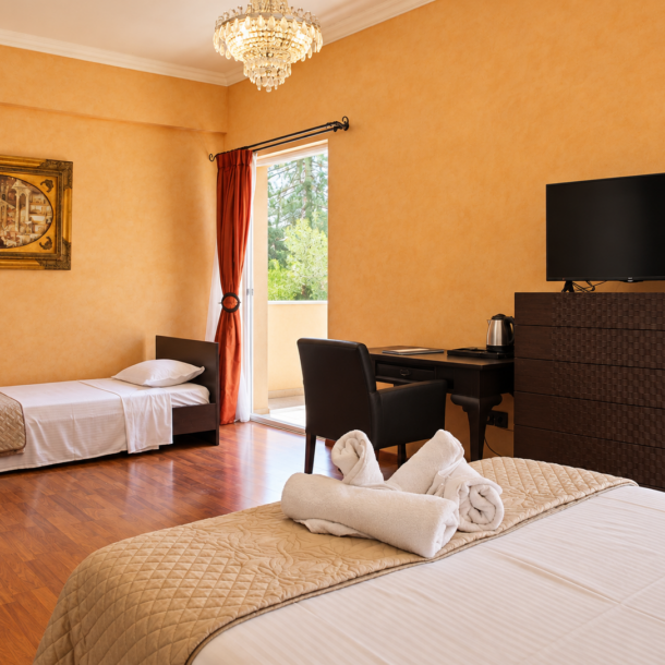 Anastazia Luxury Suites multiple-bed family room featuring hardwood floors, warm golden walls, a desk workstation, and folded white towels on premium linens