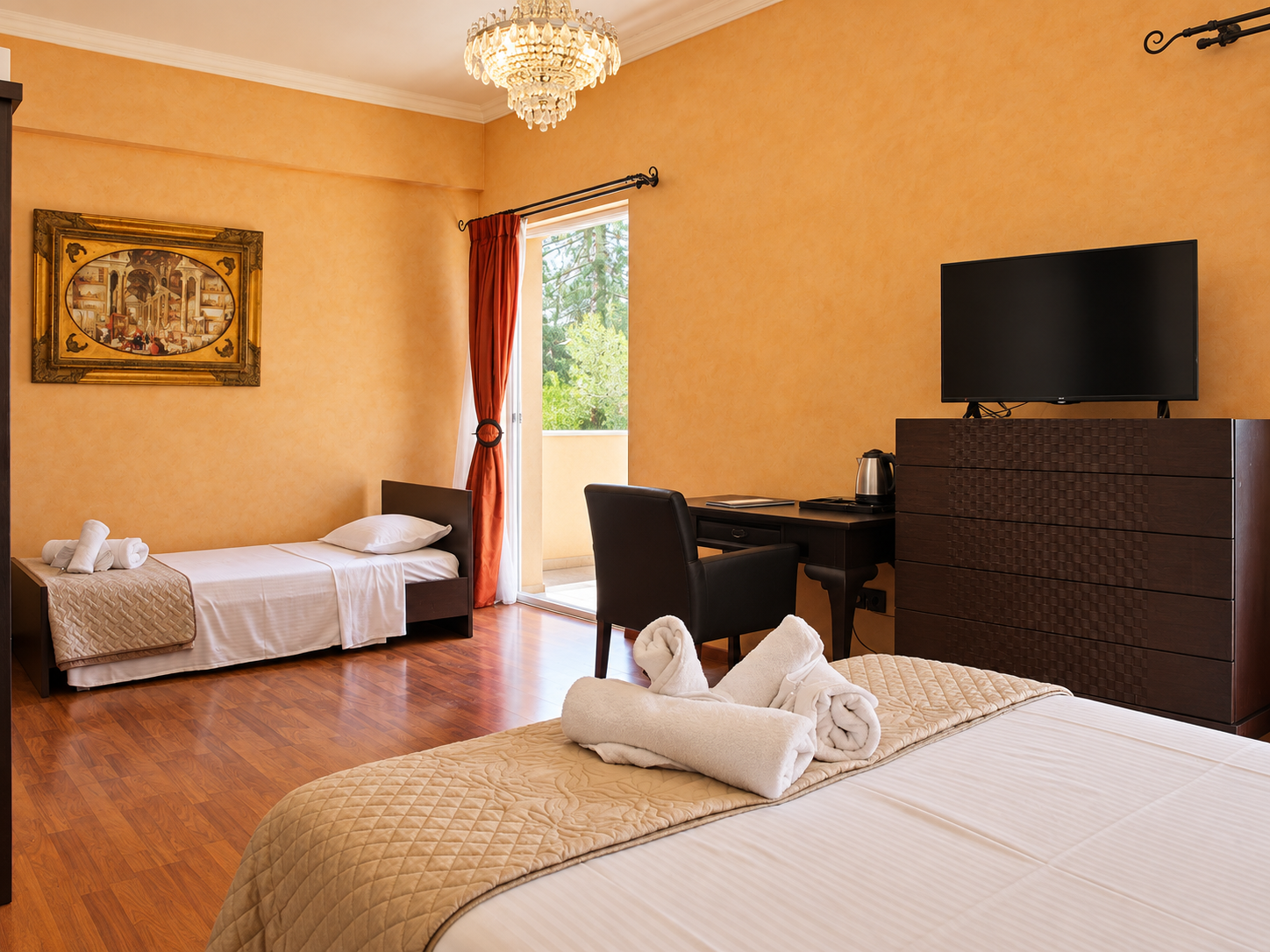 Anastazia Luxury Suites multiple-bed family room featuring hardwood floors, warm golden walls, a desk workstation, and folded white towels on premium linens