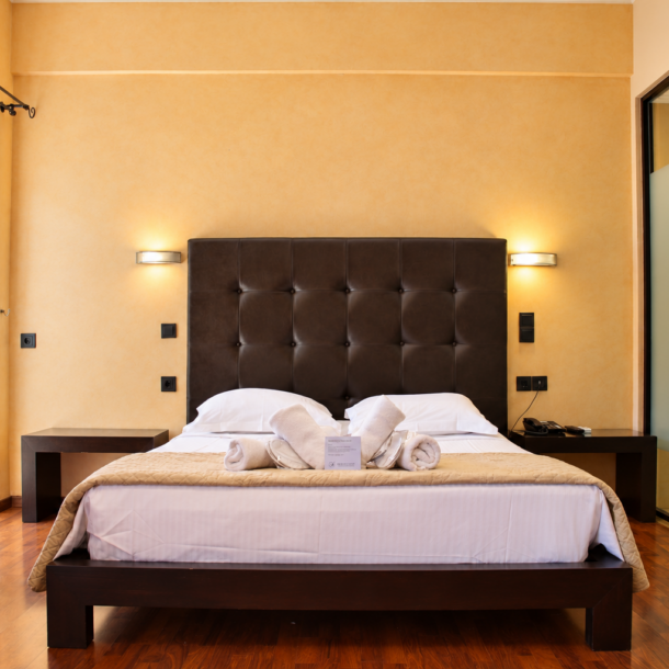 Anastazia Luxury Suites spacious family room featuring a dark tufted headboard king bed with clean white linens and a modern glass shower layout