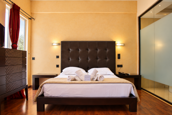 Anastazia Luxury Suites spacious family room featuring a dark tufted headboard king bed with clean white linens and a modern glass shower layout