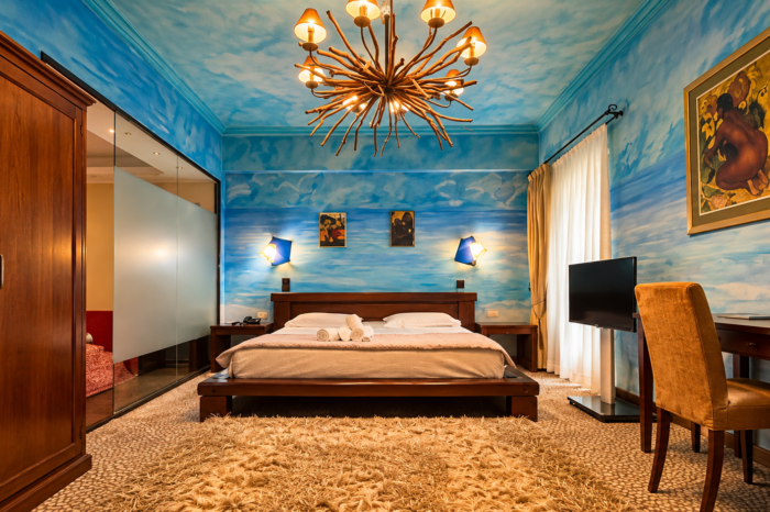 Standard Double Room with blue sky painted walls, rustic wooden bed, and branch chandelier at Anastazia Luxury Suites & Spa
